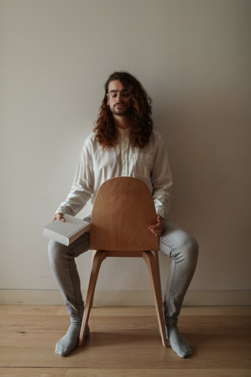 A Man Sitting on a Wooden Chair Beside a White Wall