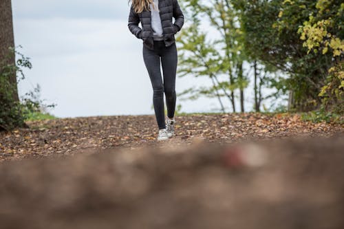 Woman in Black Leggings While Walking on Brown Road