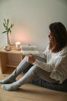 A person reading a book by candlelight in a serene indoor setting.