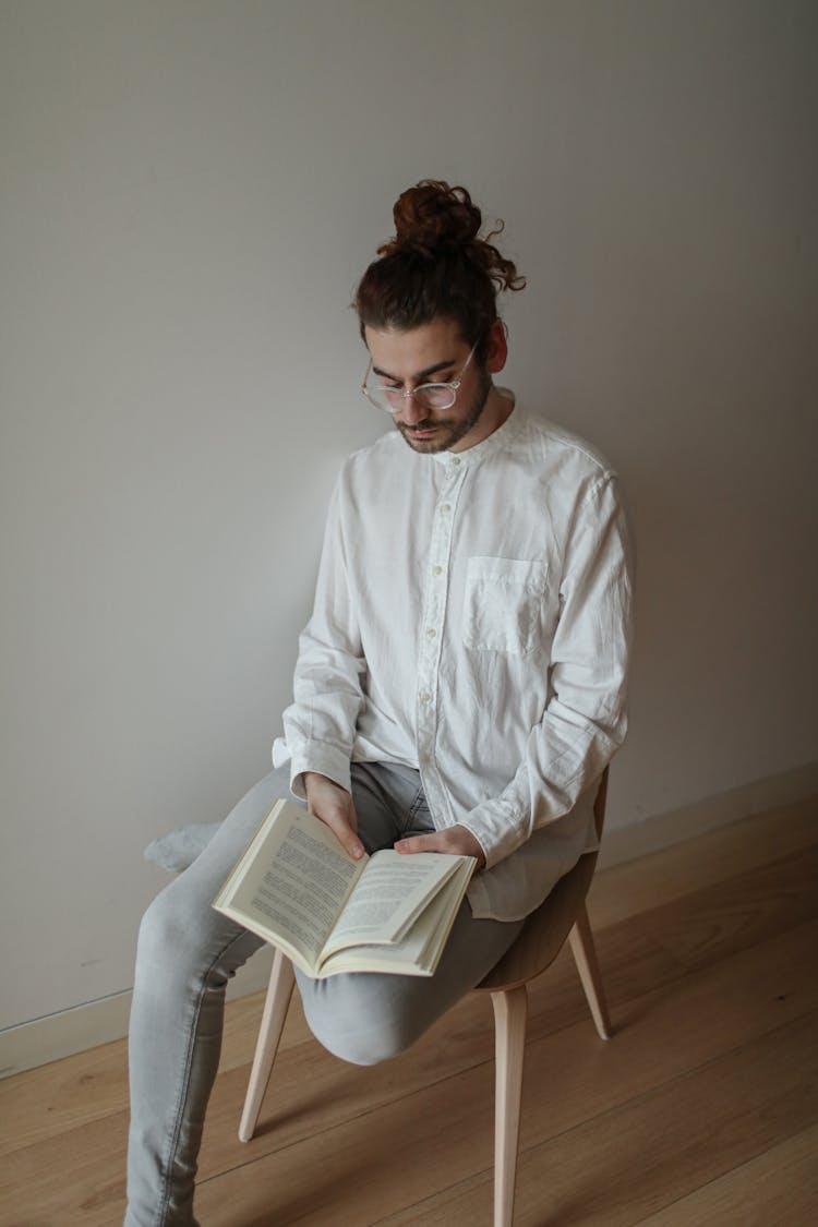 A Man In White Long Sleeves Sitting On The Chair While Reading A Book