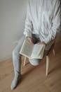 Person in White Long Sleeves and Gray Pants Holding a Book