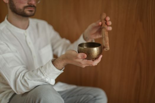 Man engaging in meditation with a Tibetan singing bowl, promoting relaxation and mindfulness indoors.