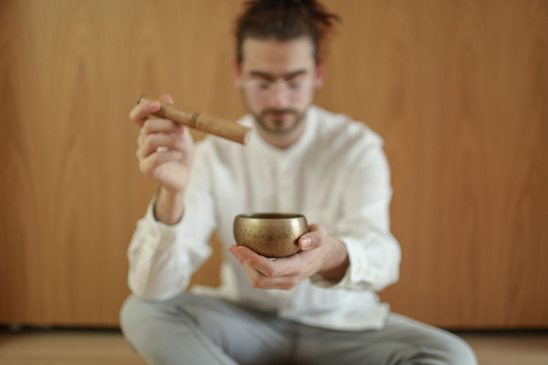 A man meditating indoors with a Tibetan singing bowl, promoting relaxation and mindfulness.