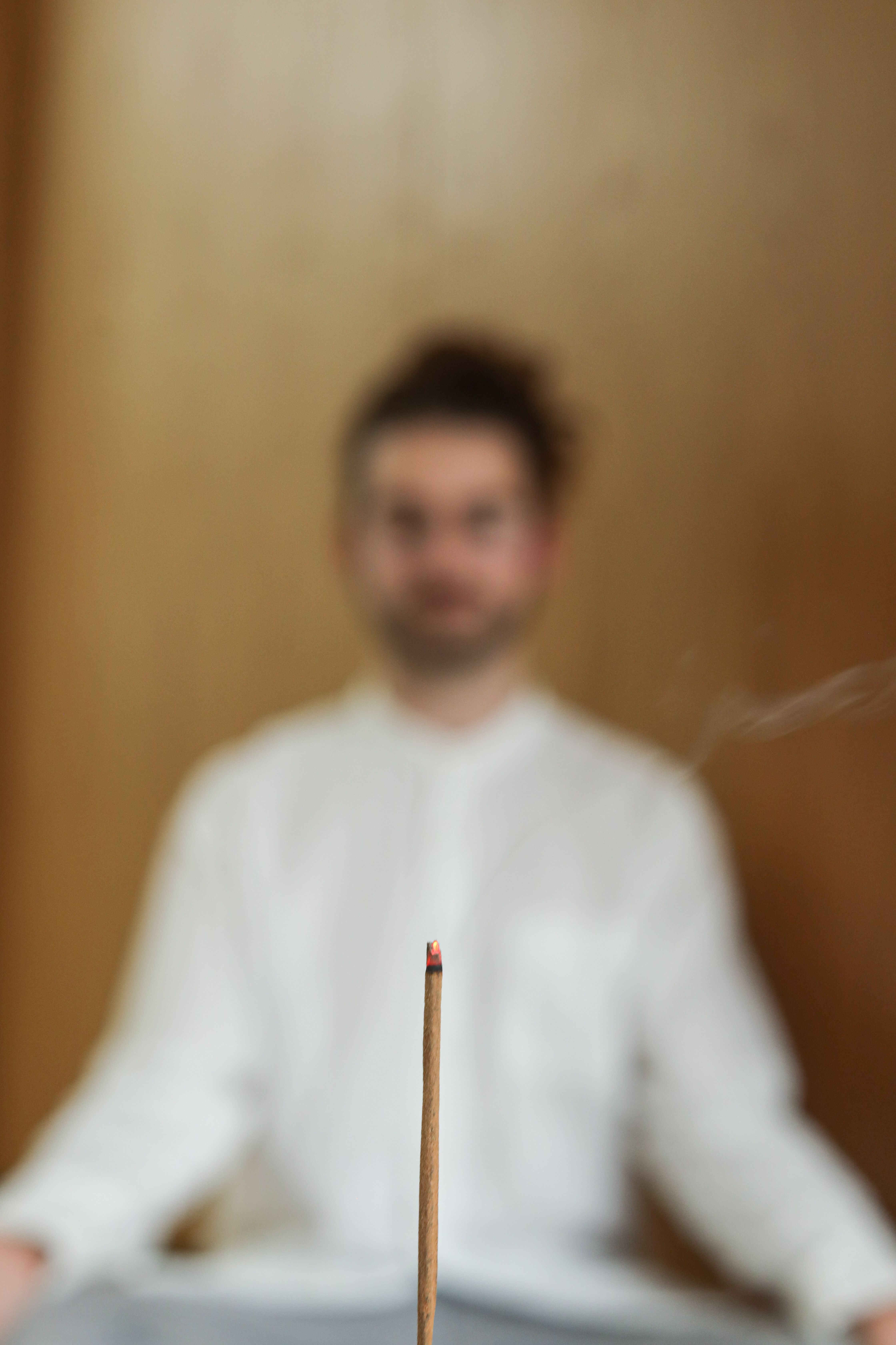 Man in meditation with burning incense stick in a peaceful indoor setting.