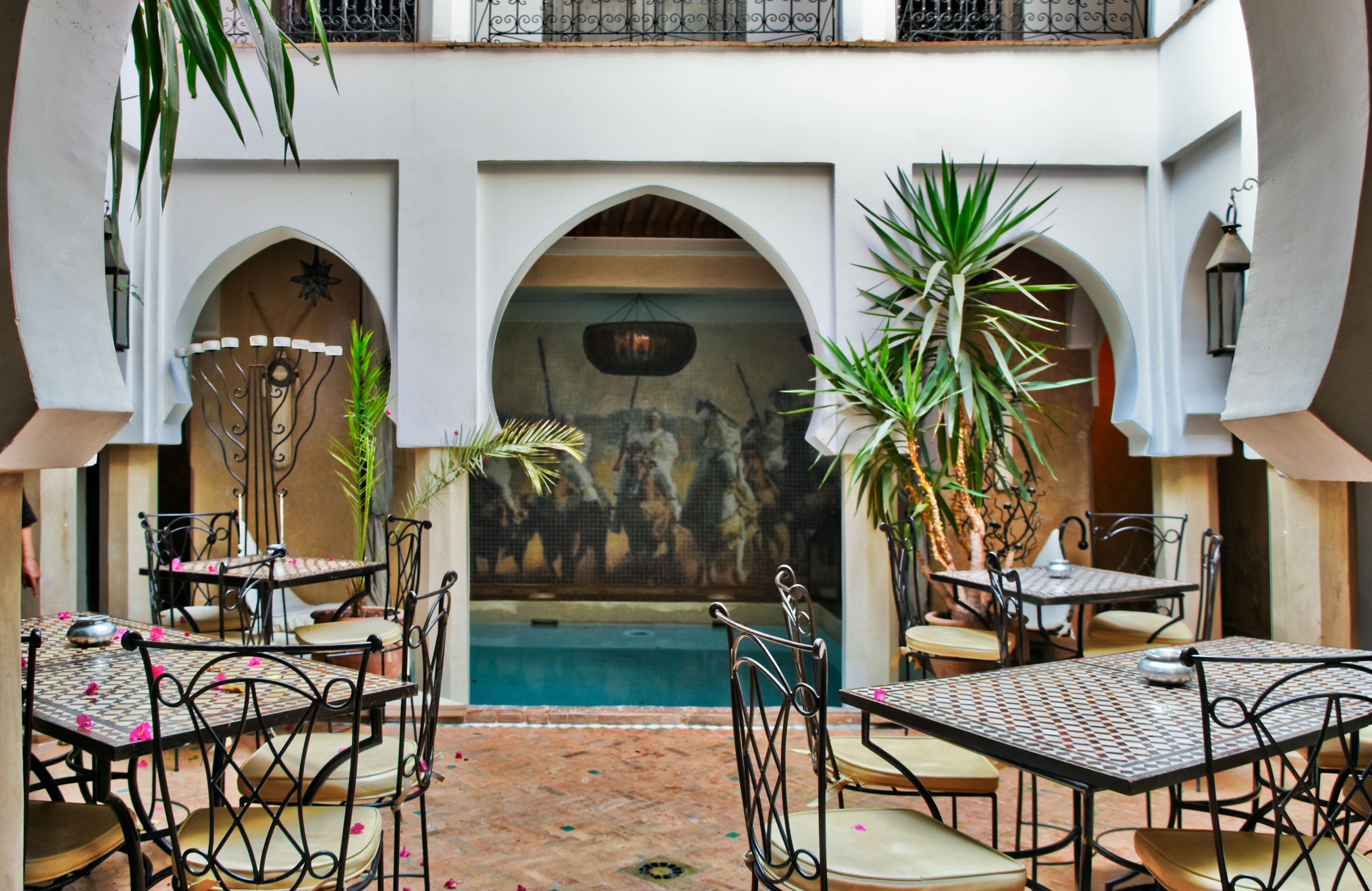 Is Marrakech Safe for Tourists? (Honest Guide) - Charming Moroccan courtyard design featuring ornate tables, chairs, and a small pool, creating a relaxing ambiance. - Marrakech