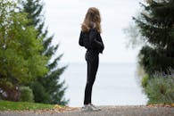 一名女子身着休闲装，站在树木环绕的小路上，俯瞰着一片水域