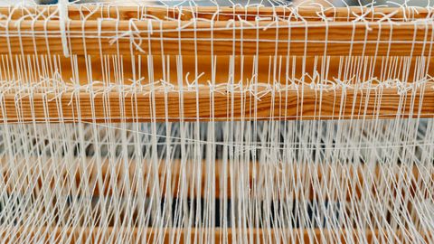 Detailed close-up of a wooden loom with white threads, showcasing traditional weaving.
