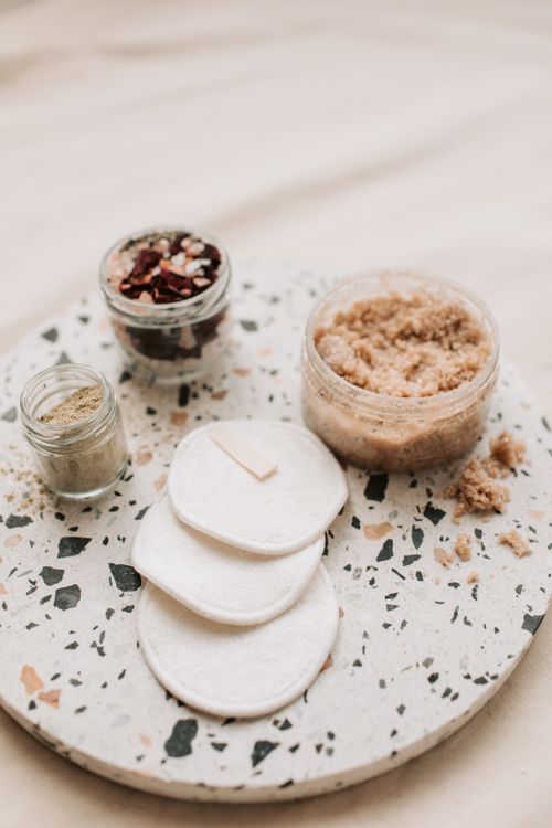 Free Explore eco-friendly beauty essentials like body scrub and reusable cotton pads on a terrazzo tray. Stock Photo