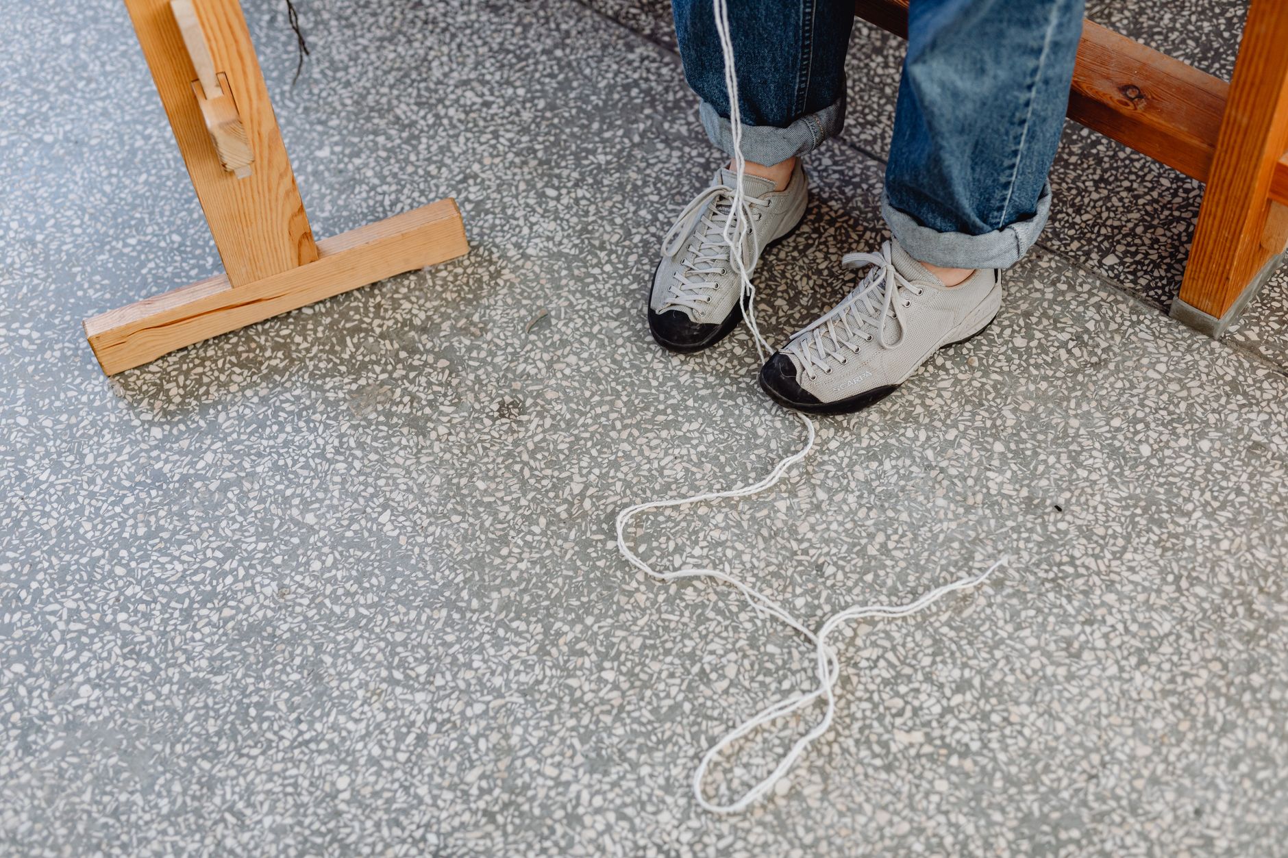 Person wearing sneakers and blue jeans with threads on a tiled floor, showcasing casual style.