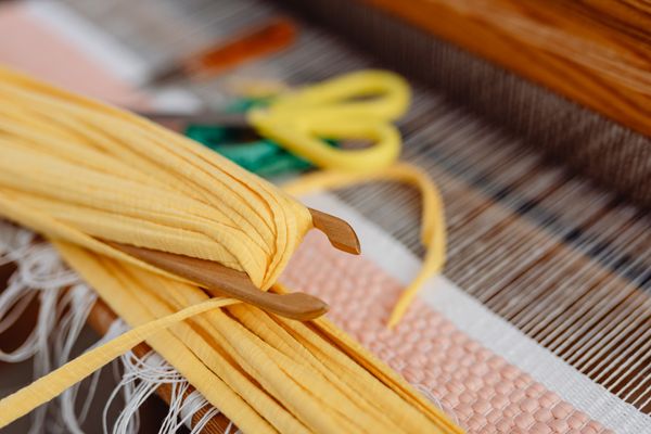 Yellow fabric and shuttle resting on a loom — photo by Kaboompics on Pexels