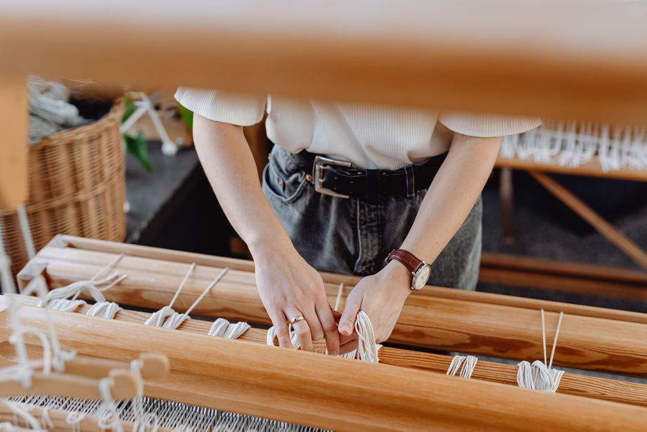 An adult woman weaving on a wooden loom, showcasing craftsmanship and focus.