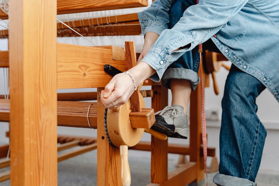 Detailed view of woman's hands weaving on a wooden loom indoors.