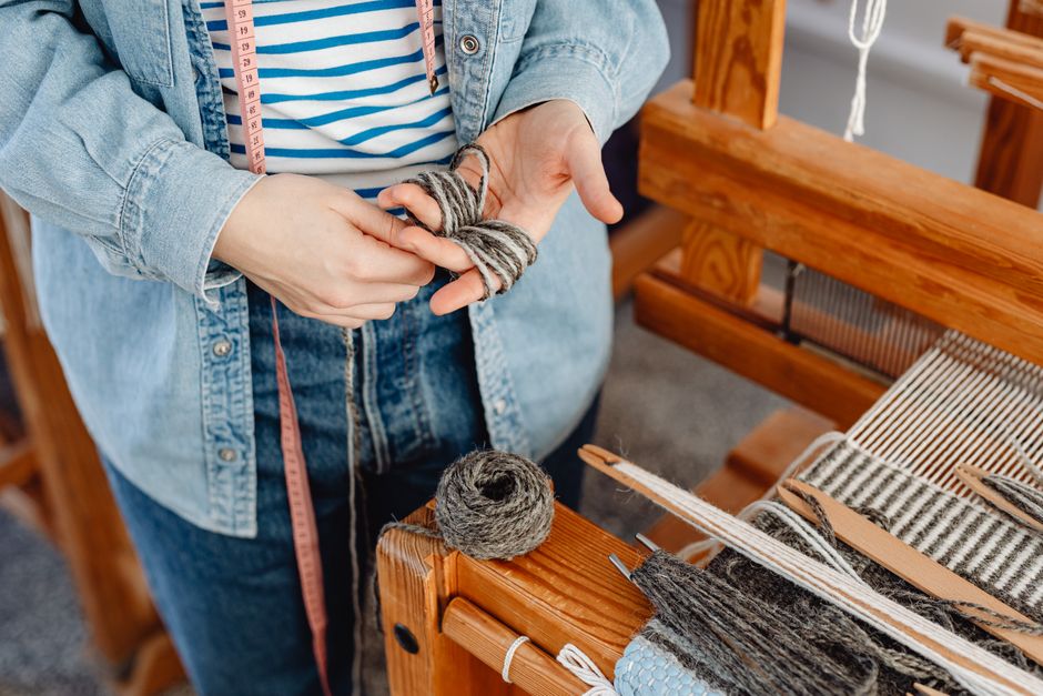 A person weaving with gray yarn on a wooden loom, showcasing detailed craftsmanship.