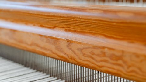 Detailed close-up image of a traditional wooden loom with white threads in focus.