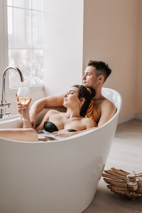 Free A couple relaxes in a bathtub with wine, enjoying a serene moment of affection and love. Stock Photo