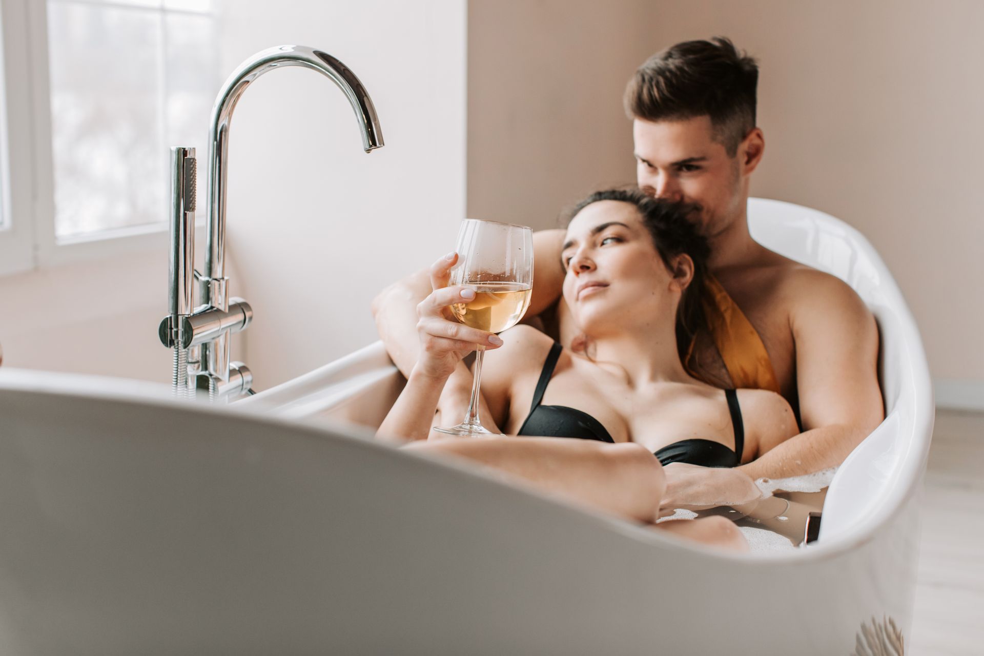 A romantic couple enjoying a relaxing bath together, sharing a glass of wine.