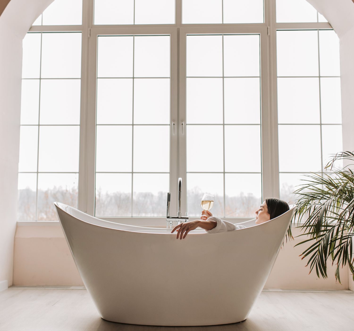 A serene scene of a woman enjoying a glass of wine while relaxing in a modern bathtub indo