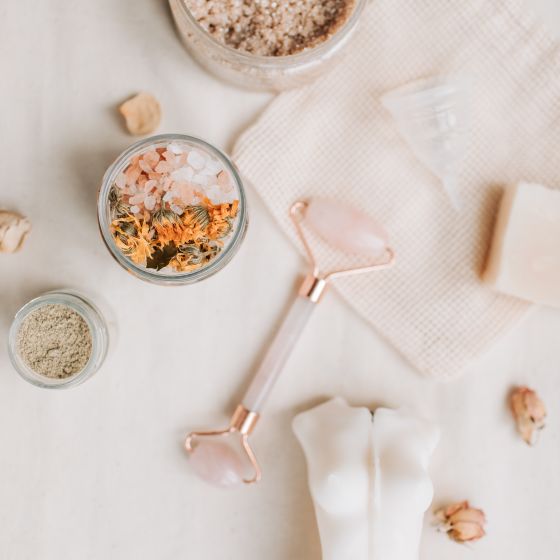 Bath salts, dried flowers and a stone roller laid out on linen. Photo by Vlada Karpovich on Pexels.