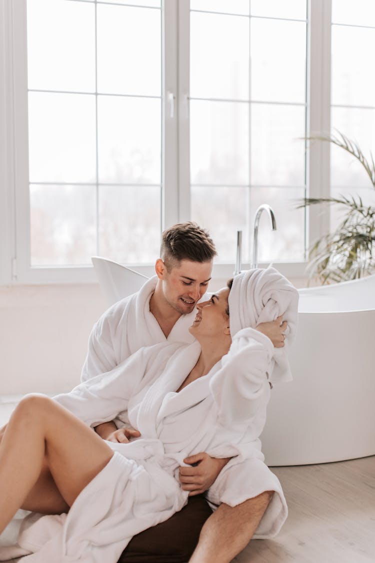 Couple In Bathrobes Sitting On Bathroom Floor