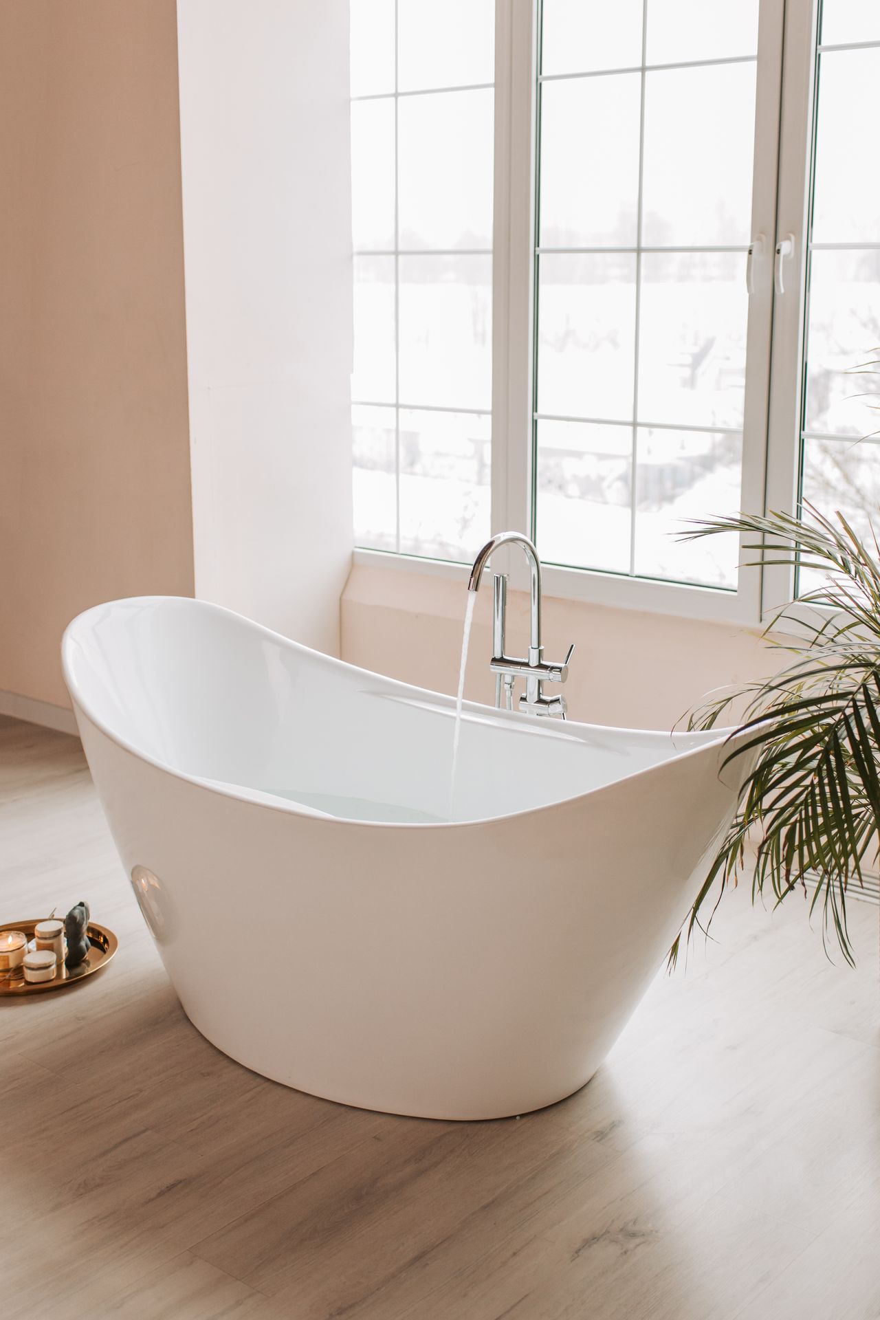 A freestanding white bathtub filling with water beside a bright window