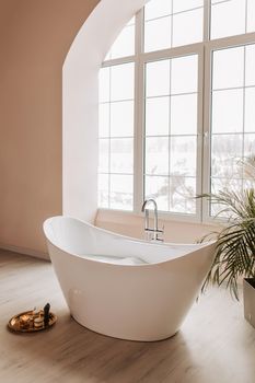 A serene modern bathroom with a freestanding bathtub near a large window overlooking a winter scene.