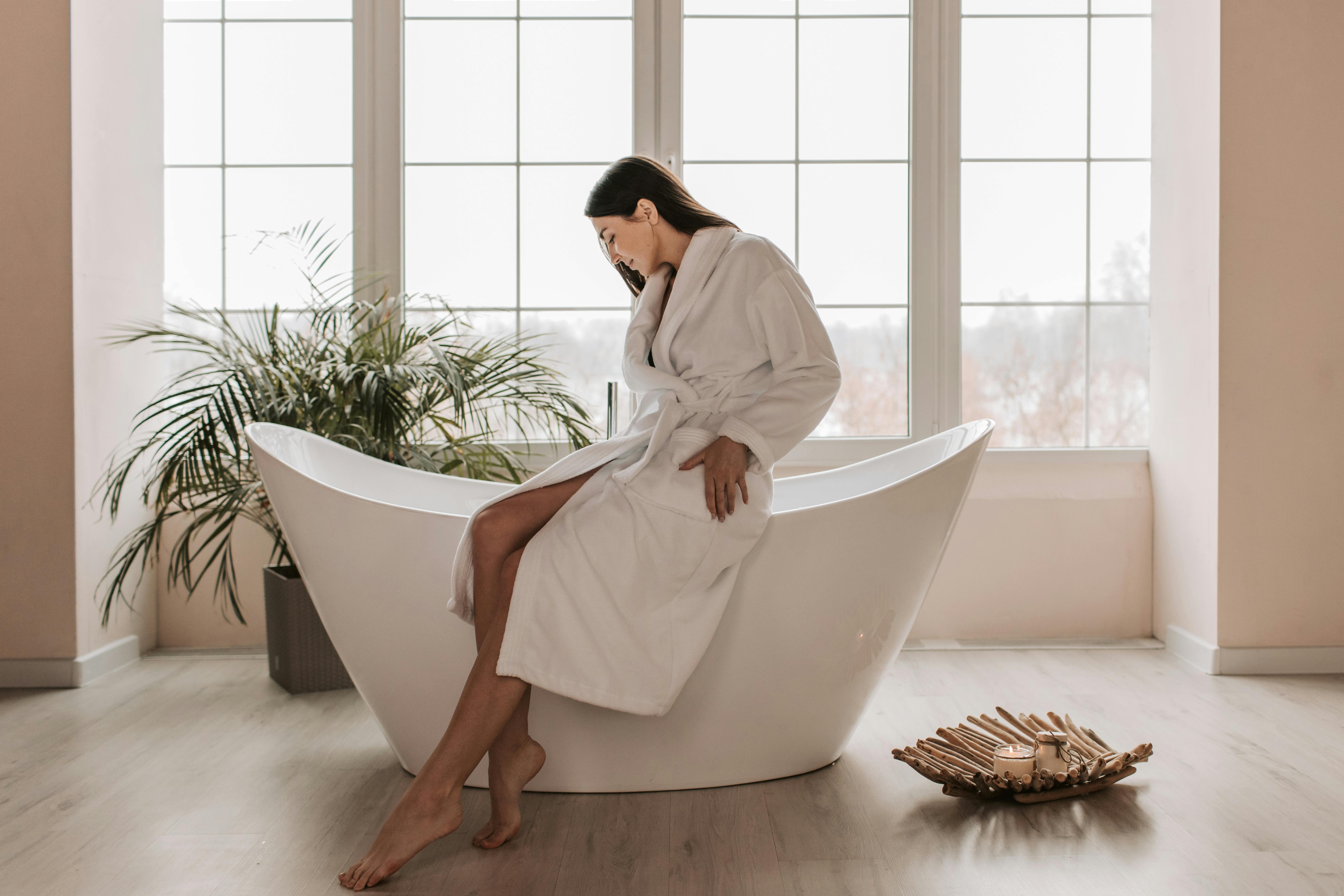 A woman sits gracefully on a modern bathtub indoors, creating a serene and peaceful atmosphere.