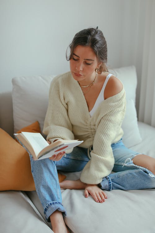 Woman Sitting on the Bed while Reading a Book
