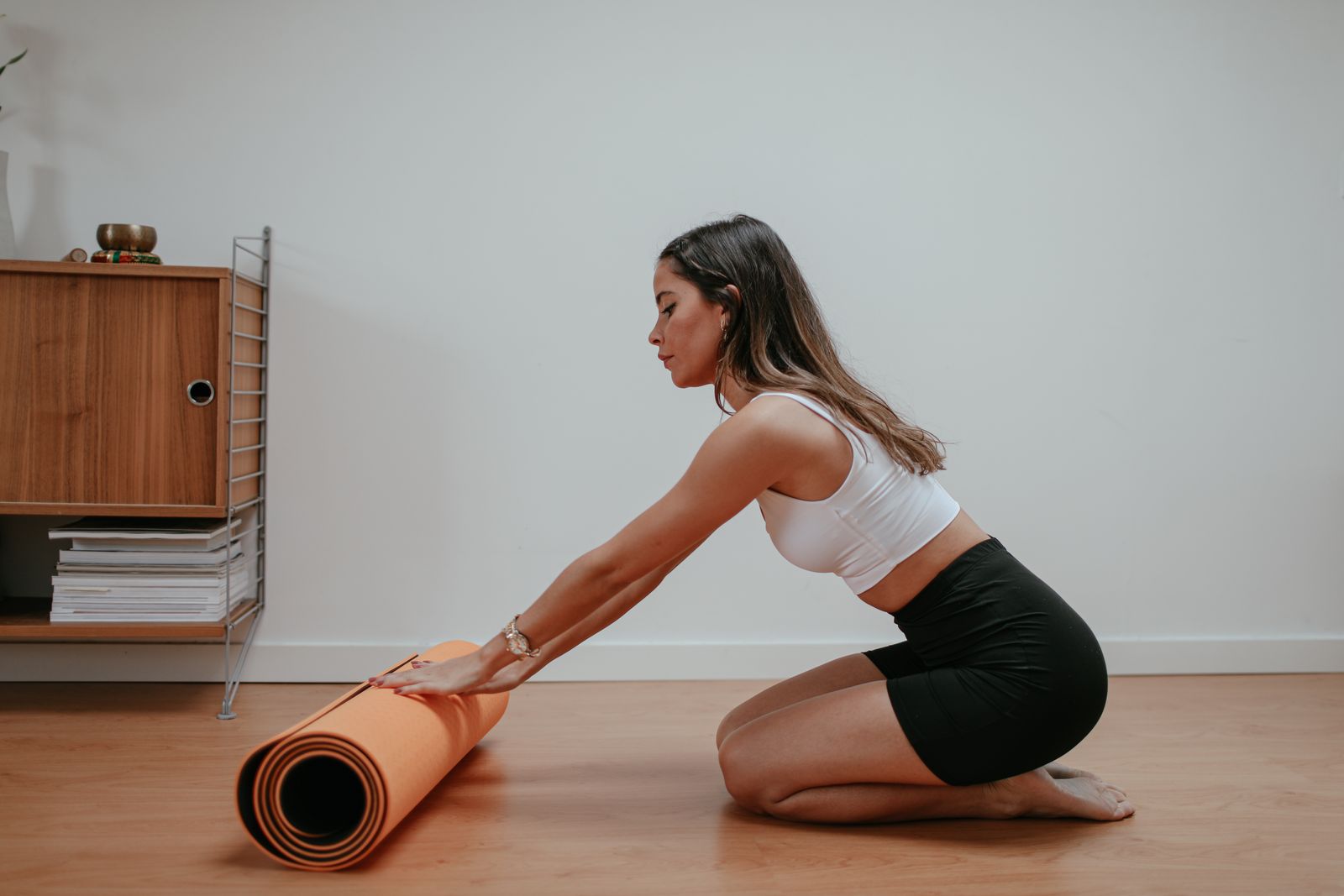 Woman rolling up an orange yoga mat in a bright modern home after practice