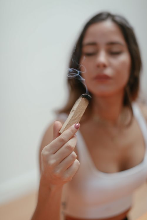 Free A woman meditates while holding burning Palo Santo indoors, creating a calming atmosphere. Stock Photo