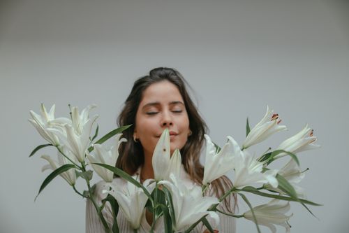 Free A peaceful woman with closed eyes holds white lilies against a plain background, embodying tranquility. Stock Photo