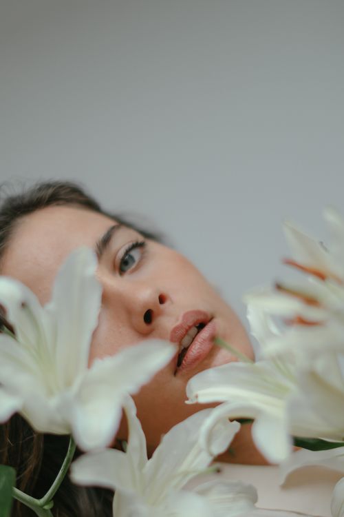 Free Captivating close-up portrait of a woman surrounded by white lilies, exuding serenity and elegance. Stock Photo