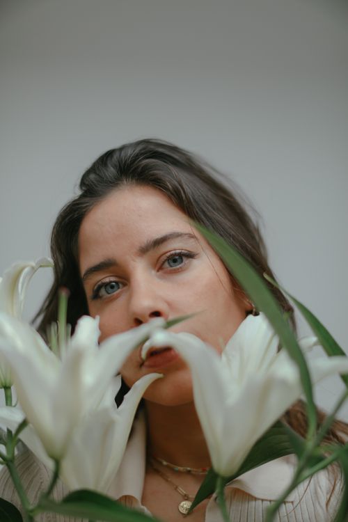 Free A captivating portrait featuring a woman behind white lilies, showcasing natural beauty and floral elegance. Stock Photo