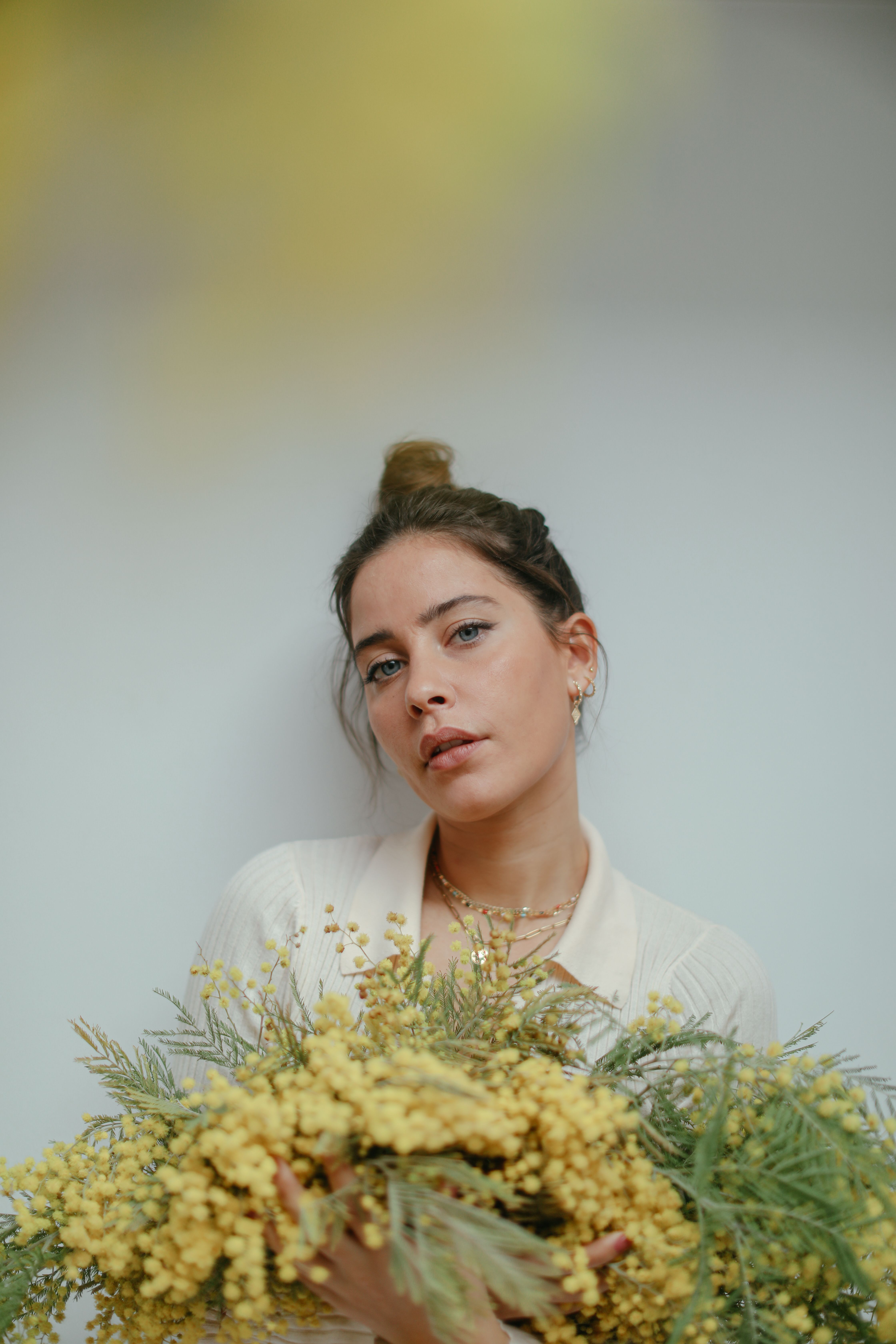 A serene portrait of a woman with a bun holding vibrant yellow flowers, soft background.