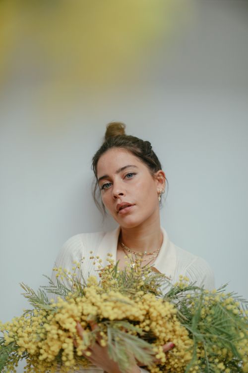 Free A serene portrait of a woman with a bun holding vibrant yellow flowers, soft background. Stock Photo