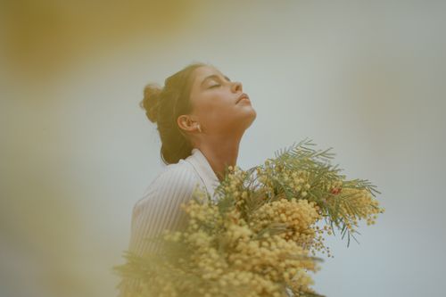 Free A serene woman outdoors holding vibrant yellow flowers amidst soft greenery. Stock Photo