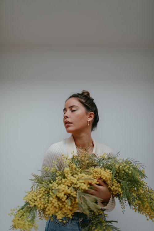 Free A serene portrait of a woman holding vibrant yellow acacia flowers indoors. Stock Photo