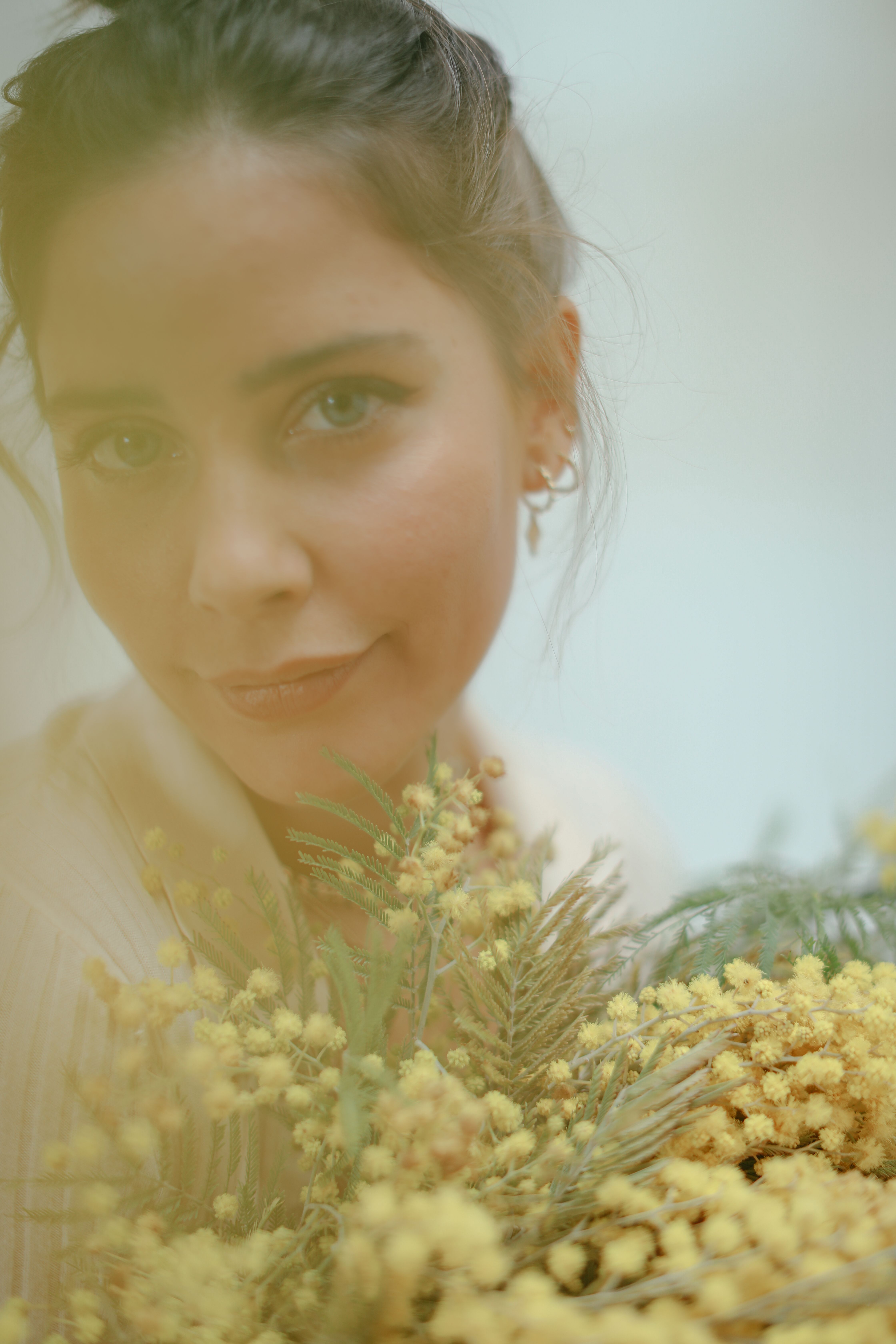 A young woman holding a bouquet of yellow flowers, captured indoors with a soft focus.