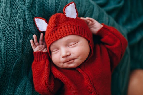 Top view of carefree little newborn baby in bright red woolen costume in plaid