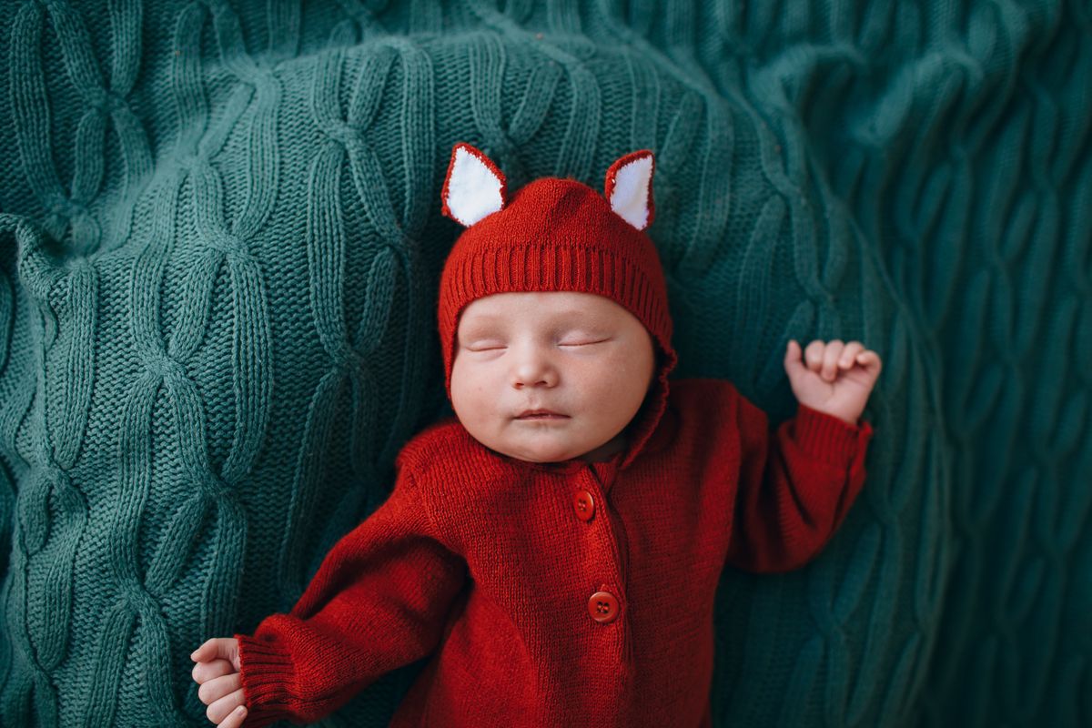 Sleeping baby in red knit clothing for first birthday photoshoot ideas