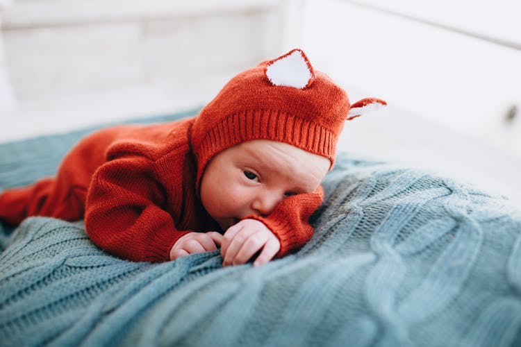 Little Funny Sleepy Baby In Knitted Costume On Blanket