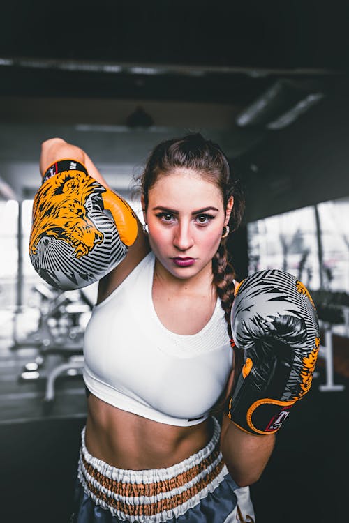 Young sporty female in bright boxing gloves with patterns on blurred background of sport club