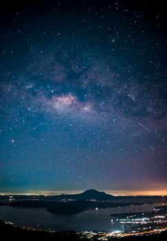 Captivating night sky over a mountaintop with city lights and visible Milky Way.