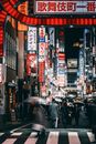 Unrecognizable pedestrians in warm clothes with umbrellas and masks strolling on city street on road with crosswalk near buildings with glowing signboards with hieroglyphs at night