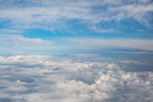 Breathtaking aerial view of of thick white cumulus and cirrus clouds floating in blue sky on sunny day