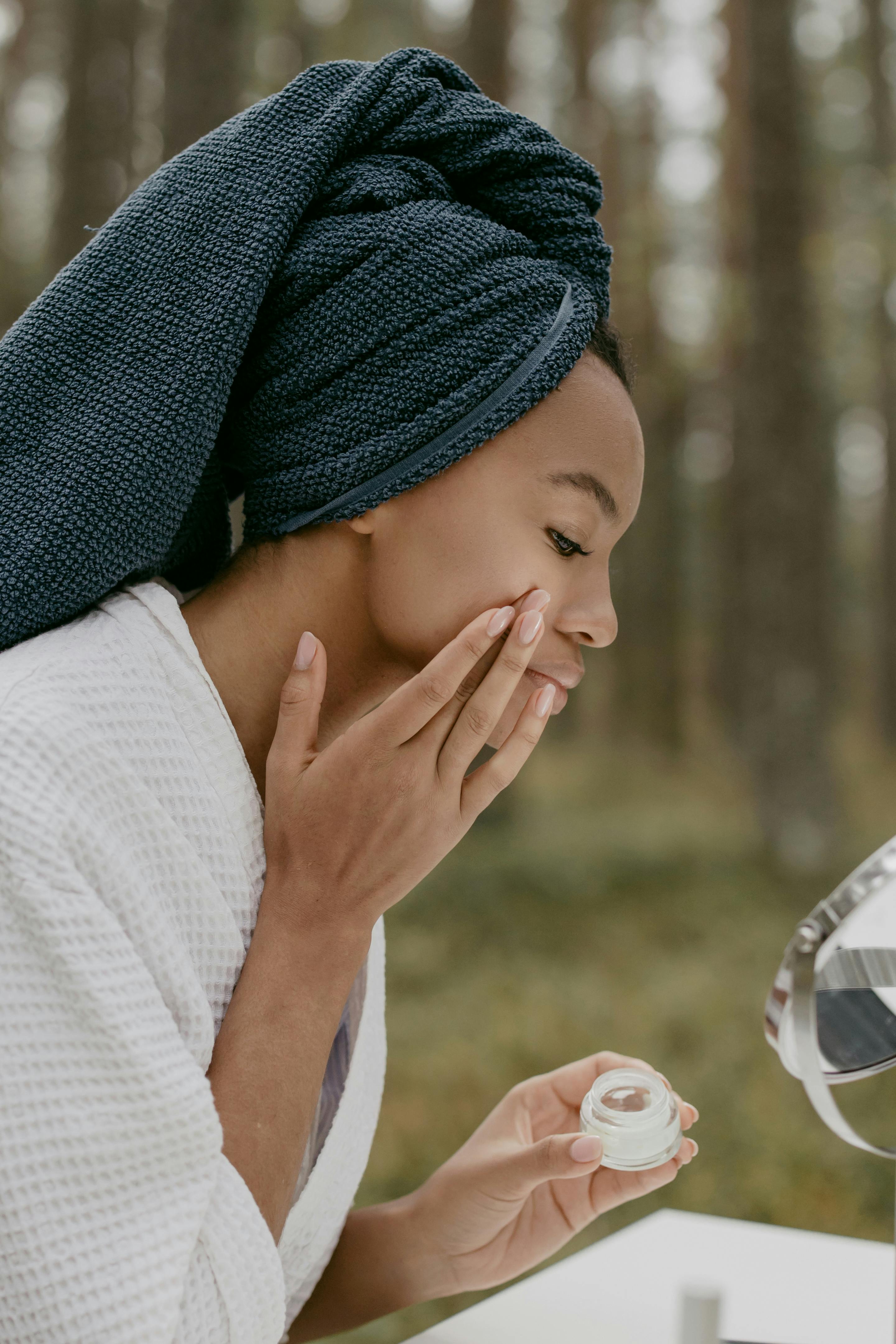 woman in white robe applying beauty product on her face