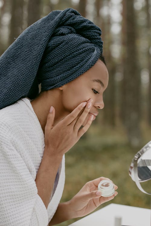 Free Woman in White Robe Applying Beauty Product on Her Face Stock Photo