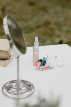 A collection of cosmetics with a mirror on a white table set outdoors, creating a serene makeup scene.