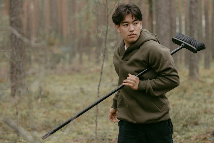 Man In Hoodie Holding A Yard Broom