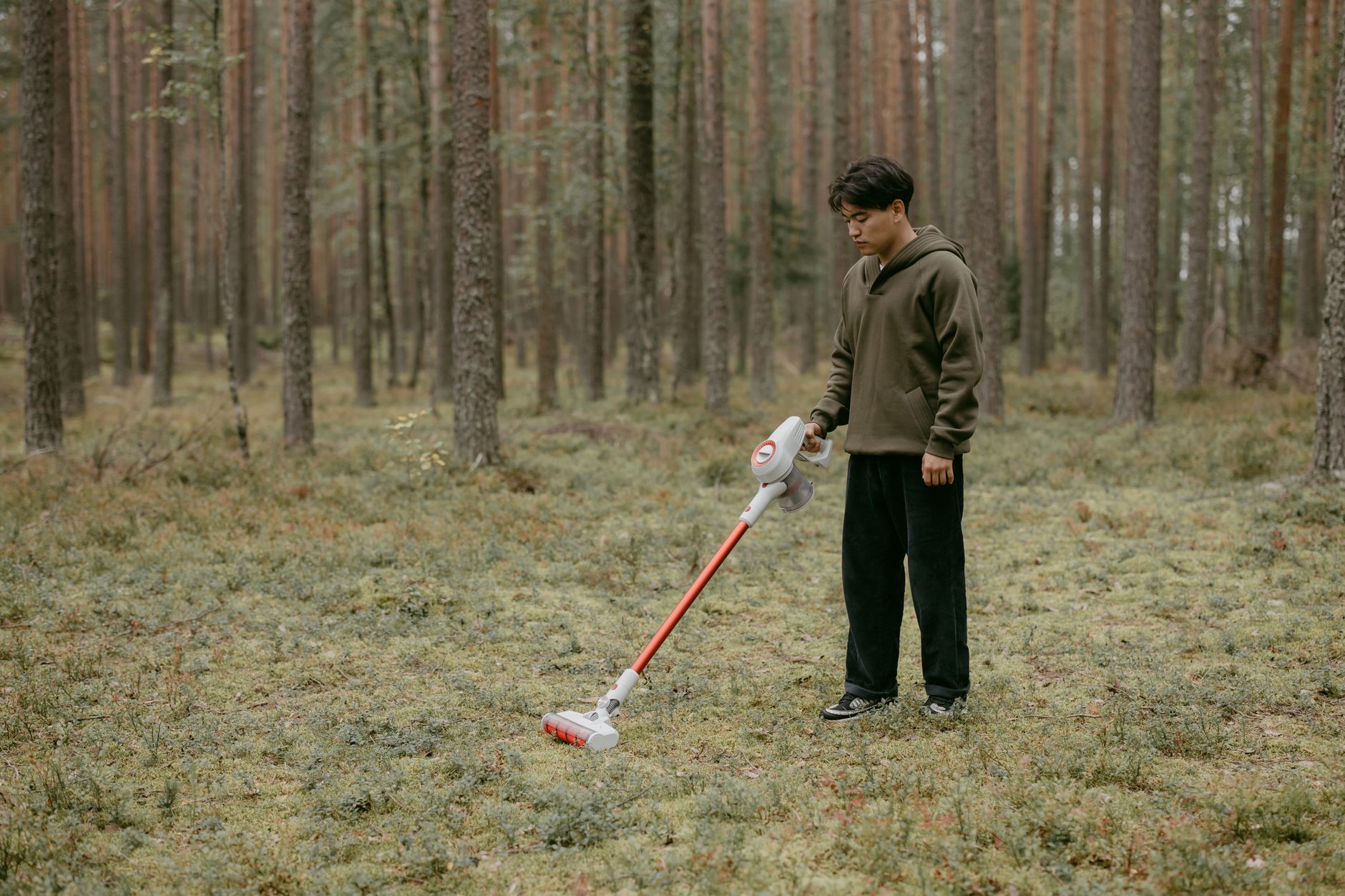 An adult man with a vacuum cleaner in a forest setting, capturing modern living concepts.