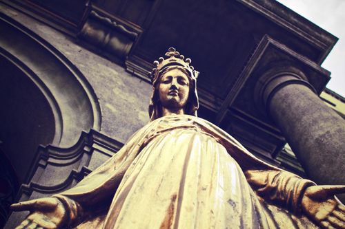 Free A golden statue of a female figure stands in front of classical architecture, exuding spirituality and elegance. Stock Photo